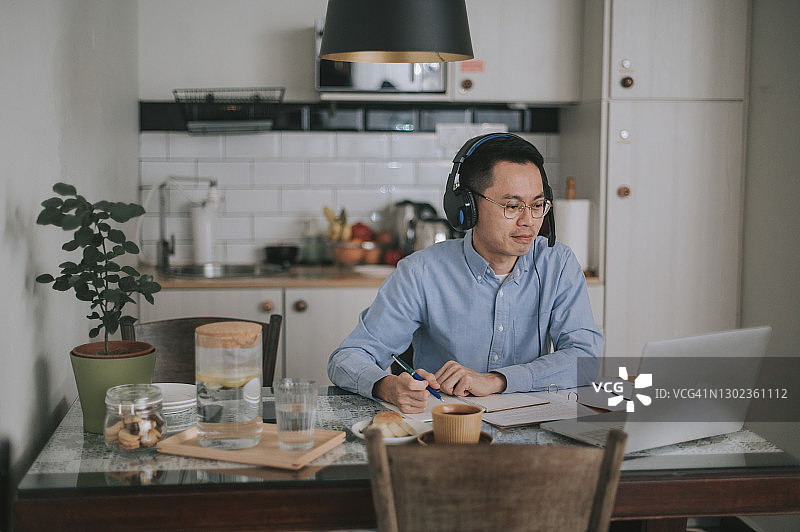 亚洲华人中年男子微笑着使用笔记本电脑在厨房上在线课程图片素材