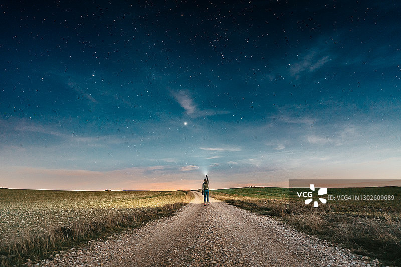 一个女人在一个晴朗的星空下走在乡间小路上，将灯笼指向天空图片素材