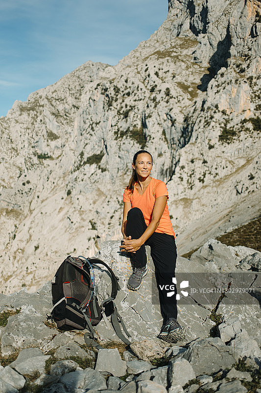 西班牙阿斯图里亚斯的Picos De Europe国家公园，一名女子背着背包坐在Cares Trail的岩石上休息图片素材
