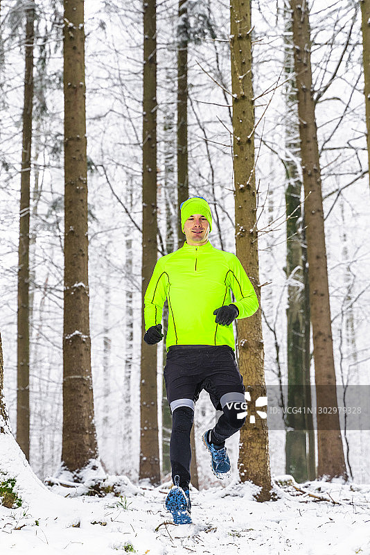 男运动员冬天在森林里的雪地上跑步图片素材