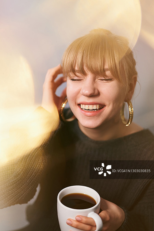 穿着毛衣戴着耳环的女孩喝着咖啡开怀大笑图片素材