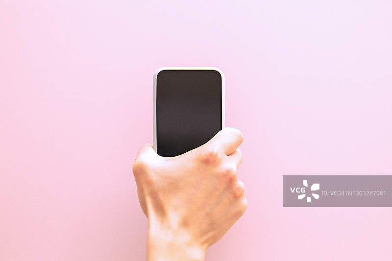 粉色背景下手持智能手机的男子图片素材