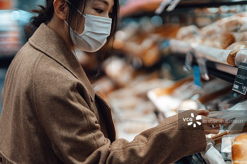 年轻的亚洲妇女戴着保护面罩在面包房购物图片素材