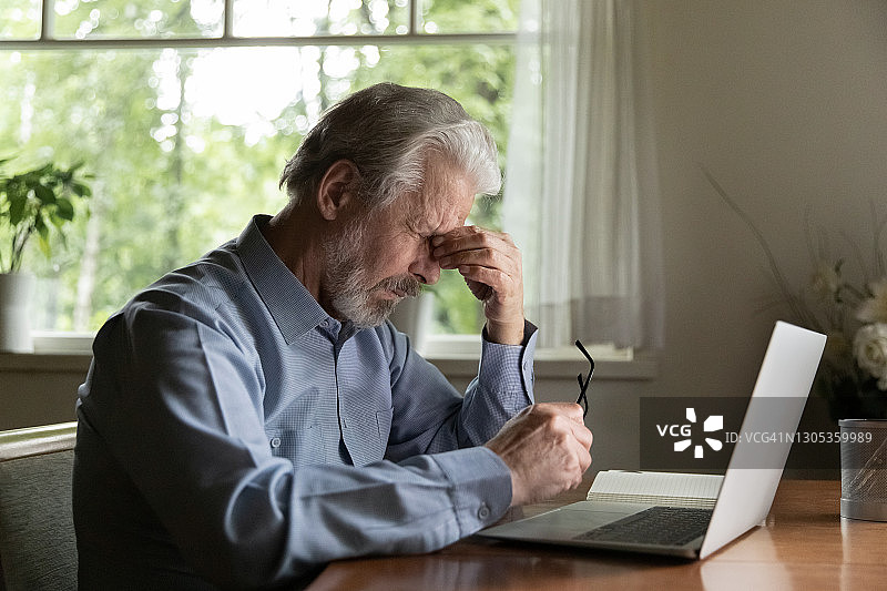 疲惫成熟的60岁男人在家用笔记本电脑工作图片素材