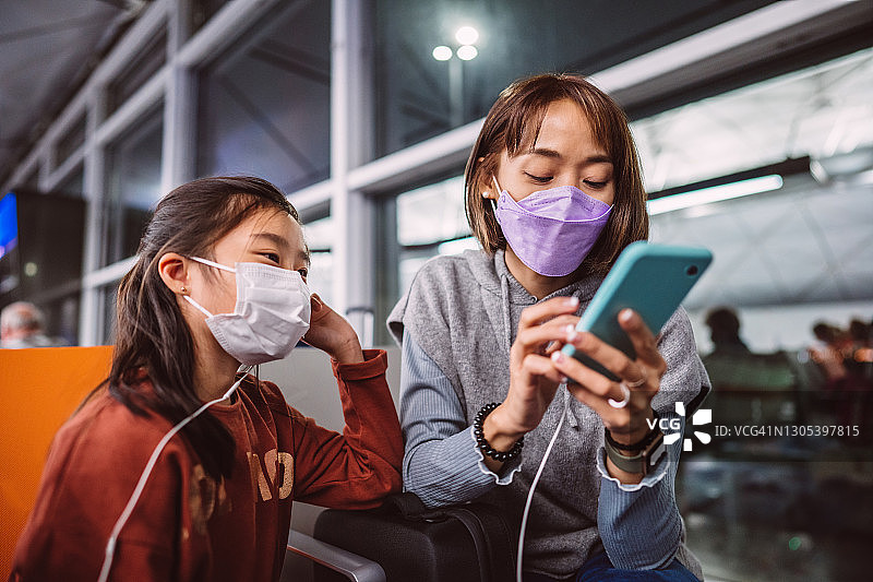 妈妈和女儿戴着防护口罩在机场用智能手机与家人视频通话图片素材