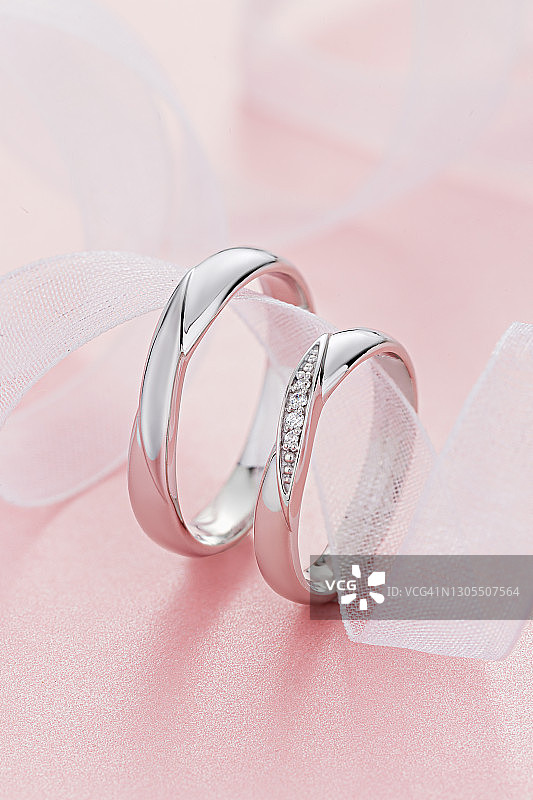 一对时尚的银色结婚戒指在粉红色的背景图片素材