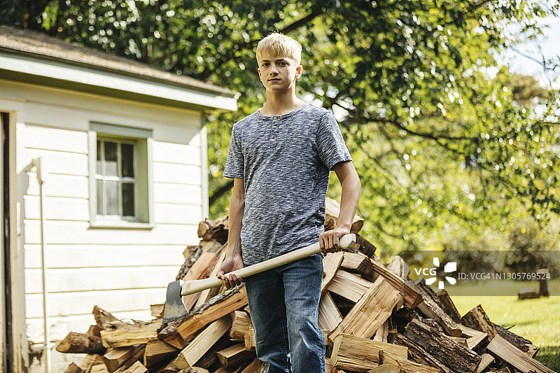 一个金发男孩拿着斧头站在一堆木头前的肖像图片素材