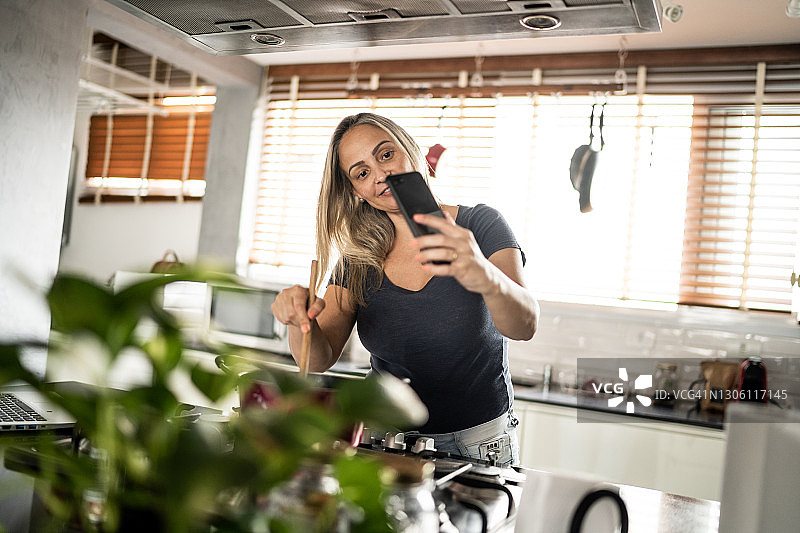成熟的女人做饭和展示食物在视频通话在家里的智能手机图片素材