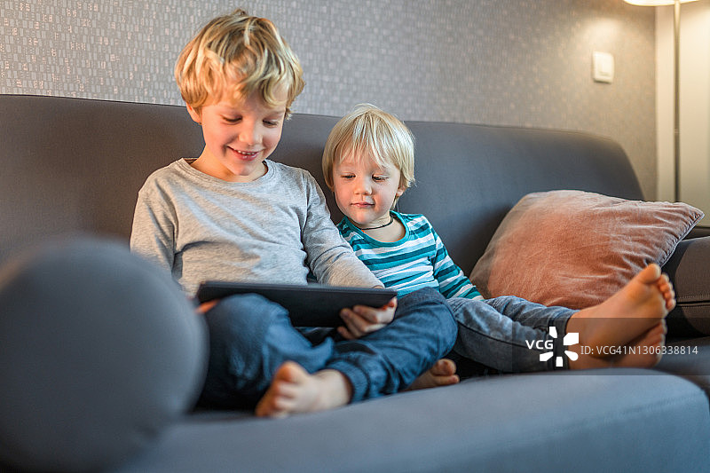 两个白人男孩坐在家里的沙发上看动画片和使用数字平板电脑图片素材