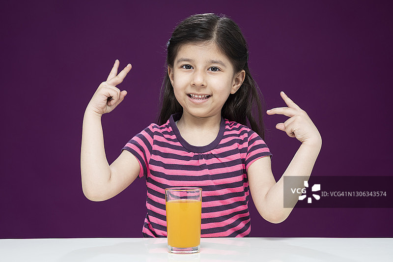 肖像印度可爱的小女孩喝橙汁，坐在孤立的白色背景:股票照片图片素材