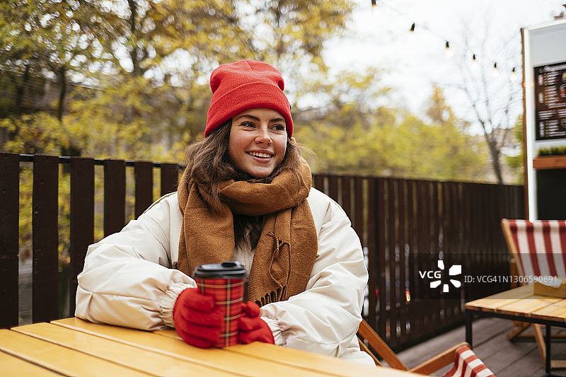 年轻女子穿着暖和的衣服坐在路边咖啡馆喝咖啡图片素材