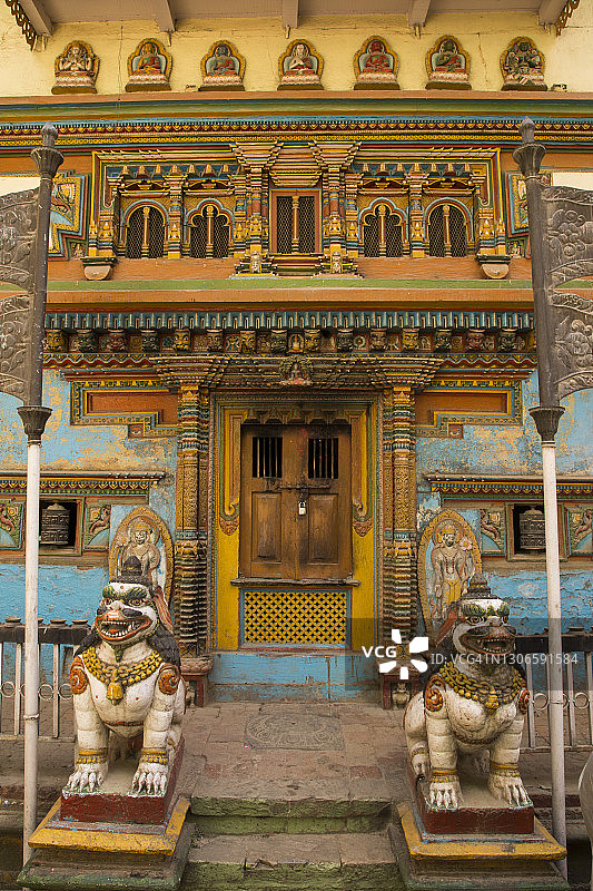 在尼泊尔加德满都的帕坦拉利特普尔，一个佛教寺庙的华丽前门，有一对守护狮子，经纶轮和华丽的木材门框和蓝色和黄色的窗户。图片素材