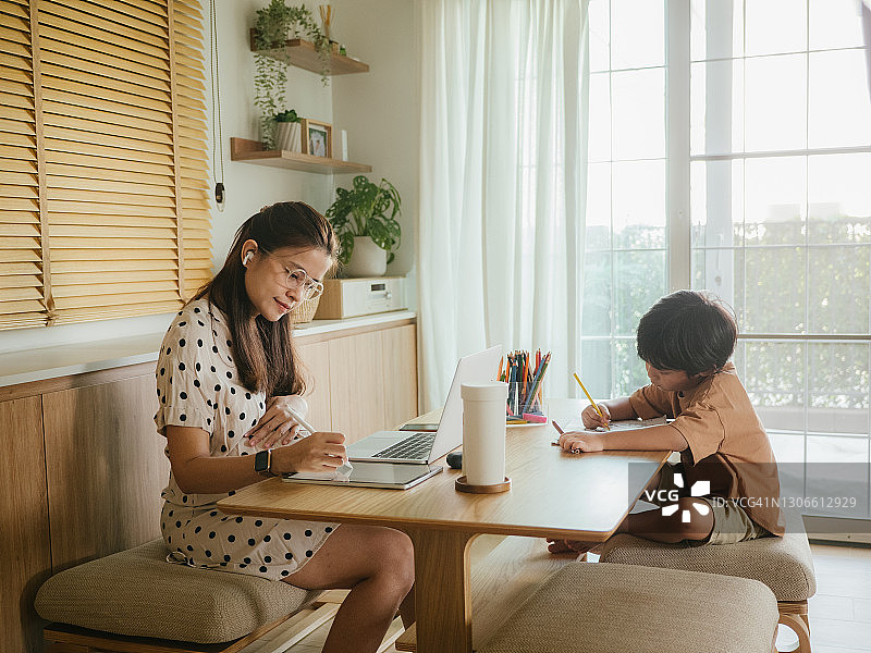 亚洲儿子在家和母亲一起参加网络课程。图片素材
