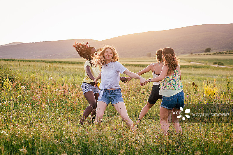 四个年轻女子手拉手围成一圈，在田地里跳着图片素材