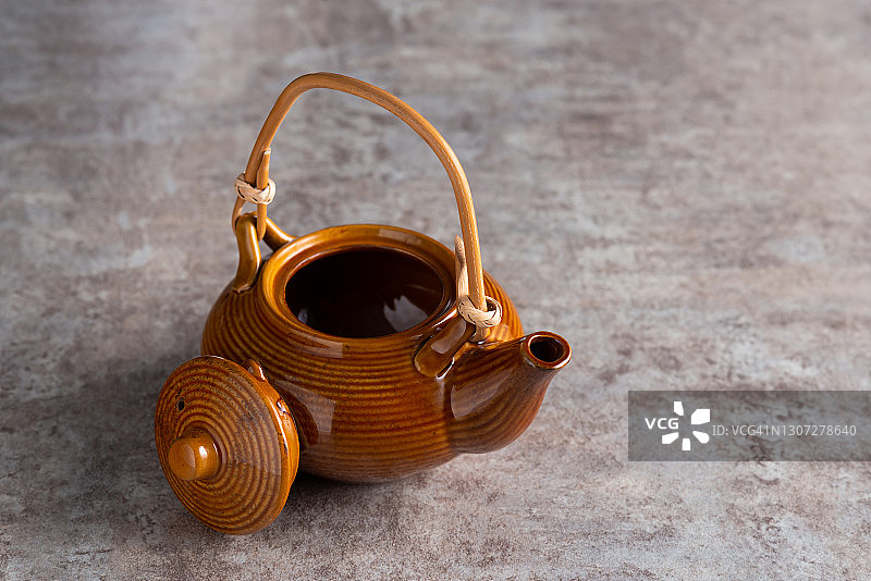 一个棕色的茶壶，竹柄和一个打开的盖子在一个石头台面上。copyspice图片素材