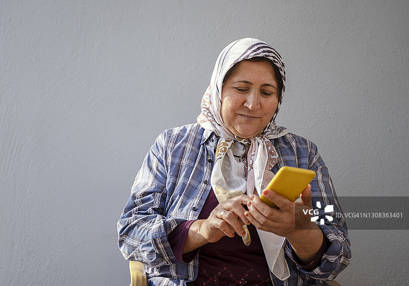 成熟的穆斯林妇女戴着头巾使用智能手机图片素材