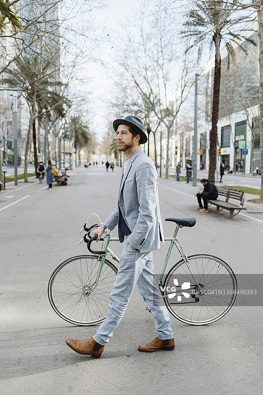 在城市里戴着帽子骑着自行车走路的职业男性图片素材