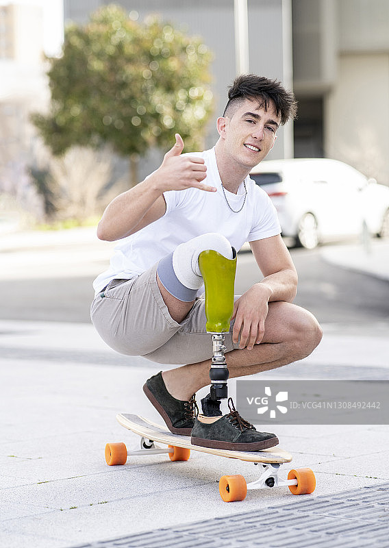 微笑的残疾人展示沙卡标志，而滑板在街上图片素材