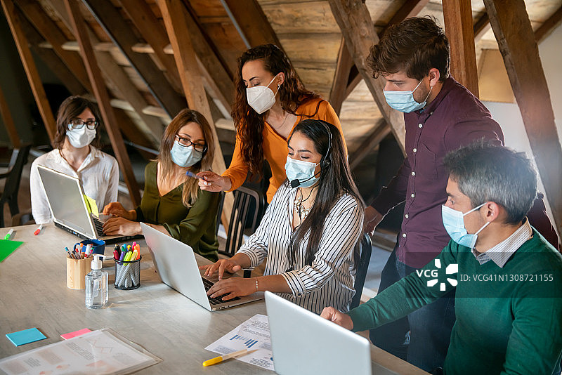 在大流行期间戴口罩在办公室共同工作的工作人员团队图片素材