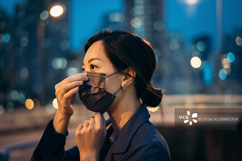 年轻的亚洲妇女戴上防护面罩，以保护和防止病毒在城市中传播，抵御夜晚城市灯光的照射。日常生活的新常态图片素材