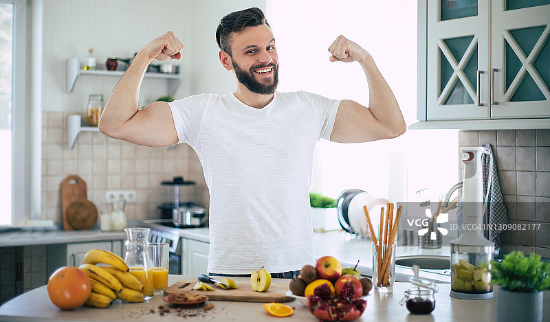 英俊的年轻运动微笑的男人在厨房准备素食健康的水果沙拉和冰沙在一个好心情图片素材