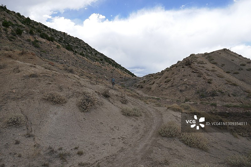 远处的自行车手骑着山地车爬上陡峭的土路图片素材