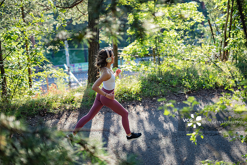 年轻的女运动员慢跑穿过森林。图片素材