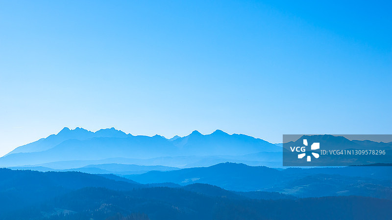 蓝色超现实的山脉映衬着青色的天空，梦幻般的童话般的山景图片素材