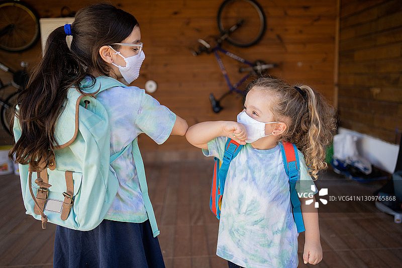 2019冠状病毒病期间，姐妹们戴着防护口罩准备上学。新常态图片素材