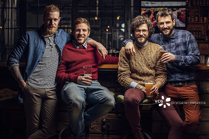 一群快乐的男人在酒吧喝啤酒的肖像，看着相机图片素材