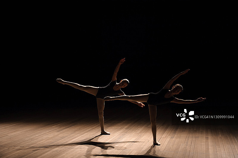 柔韧的芭蕾舞演员在昏暗的灯光下伸展四肢。图片素材