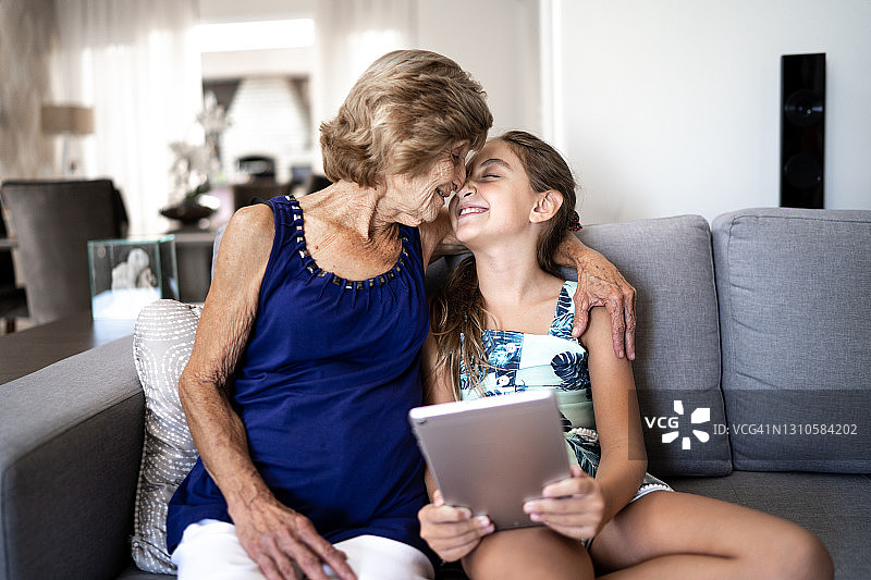 祖母和孙女在家里用平板电脑时擦鼻子图片素材
