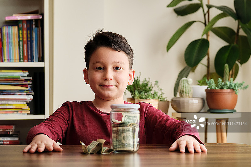 孩子在家里用玻璃罐子存钱图片素材