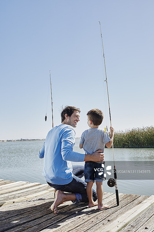 微笑的父亲看着儿子站在码头上的鱼竿图片素材