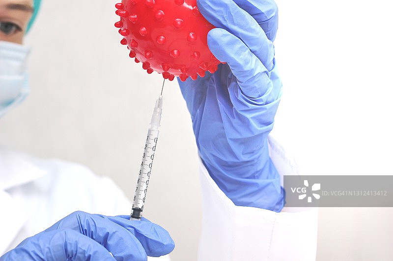 一位戴着一次性手套的医务工作者手持一个冠状病毒的抽象模型和一个注射器图片素材
