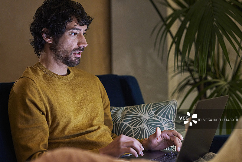 穿毛衣的男人在家里用笔记本电脑图片素材