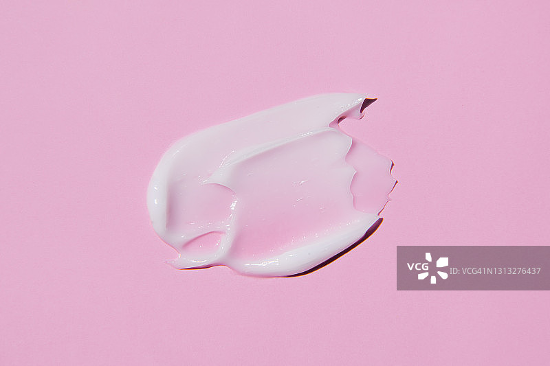 粉红色背景上孤立的白色奶油液体状涂片。图片素材