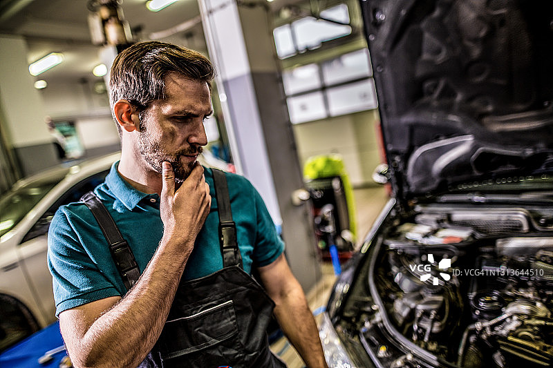 担心的机修工在汽车修理厂检查发动机问题。图片素材