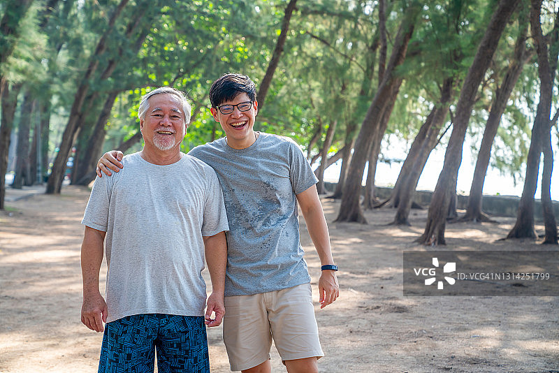 夏天的早晨，亚洲的老父亲和成年的儿子一起在海滩上做运动。图片素材