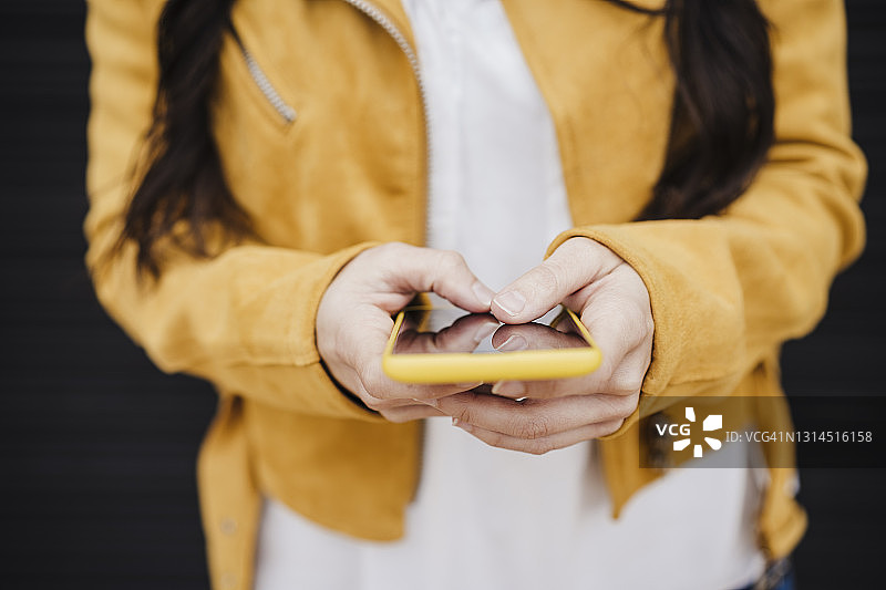 穿着黄色夹克的中年女性通过智能手机发短信图片素材