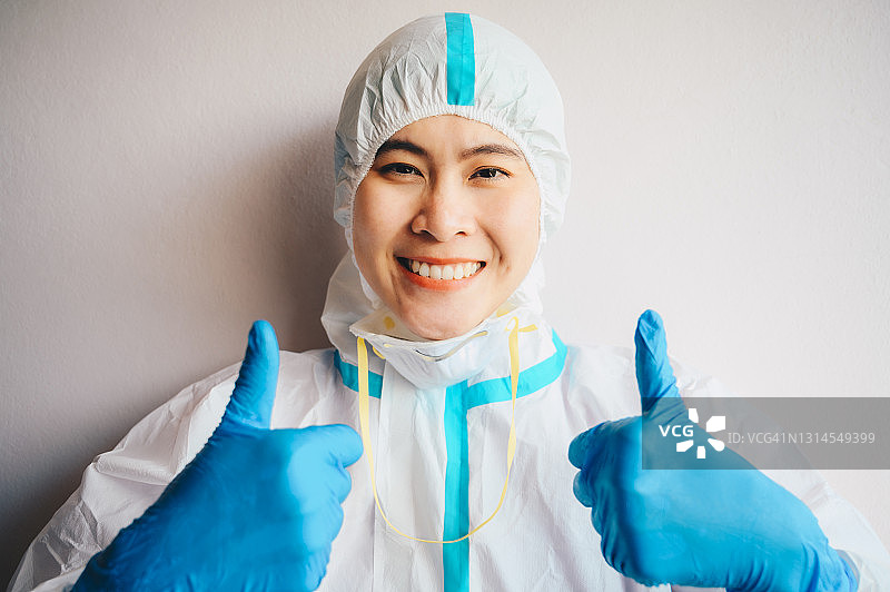 2019冠状病毒病大流行期间，身着防护服的年轻快乐医护人员在医院工作时竖起大拇指。图片素材