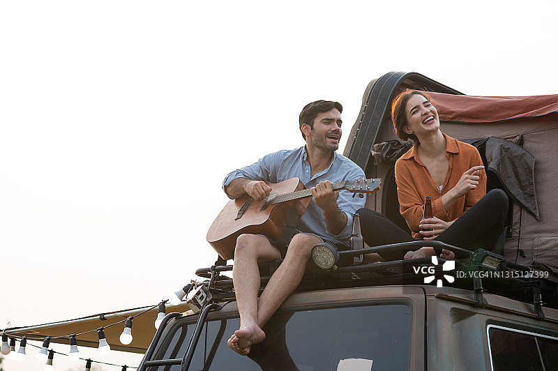 一对年轻的情侣喜欢在车顶帐篷上弹吉他图片素材