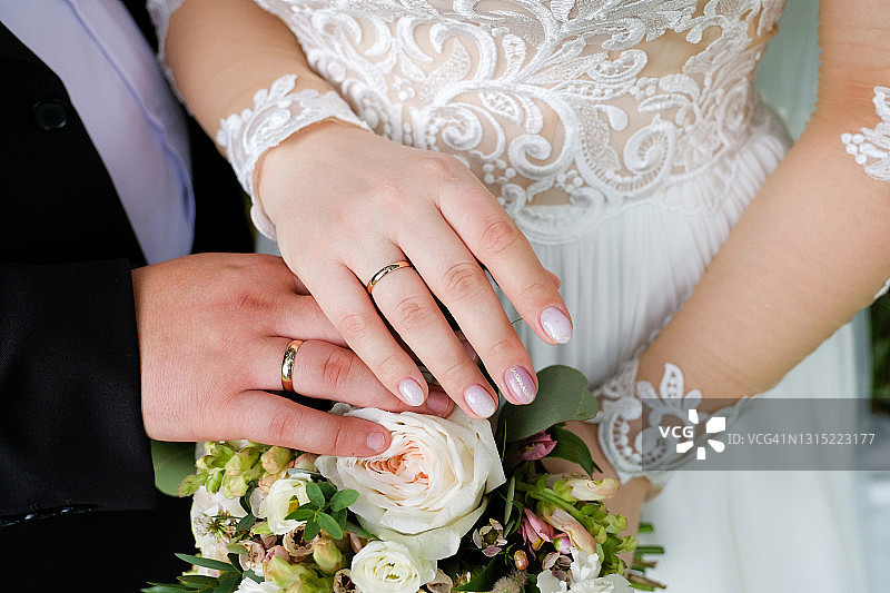 新郎和新娘的手捧一束玫瑰和绿叶。结婚戒指戴在新婚夫妇的手指上。图片素材