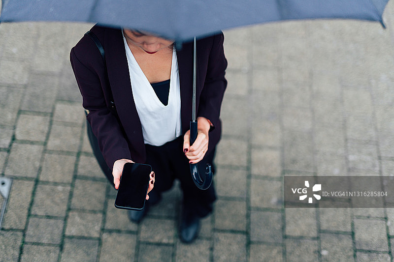 商业女性在雨中使用智能手机的镜头图片素材