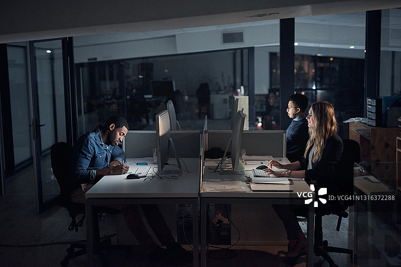 这是一群年轻的商人在深夜使用他们的电脑在一个现代化的办公室图片素材
