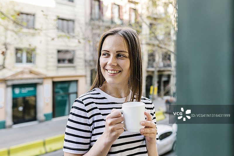 微笑的女人看着别处，同时拿着咖啡杯在阳台图片素材