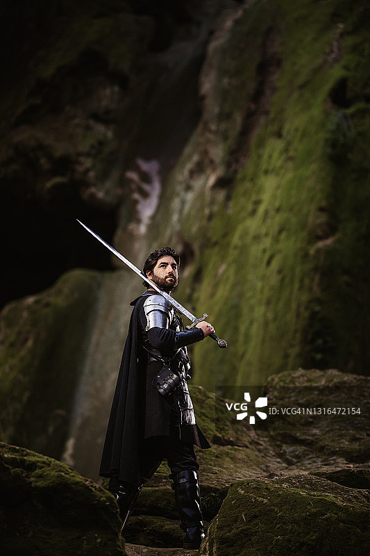 黑色幻想战士手持剑站在长满青苔的岩石前抬头仰望图片素材