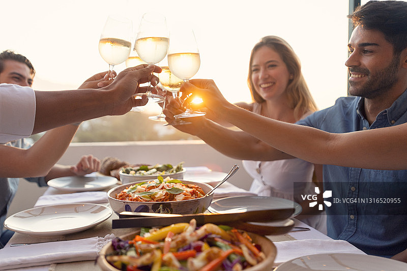 一群朋友在户外用餐。他们用白葡萄酒祝酒庆祝。图片素材