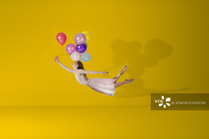 快乐的芭蕾舞演员在黄色的背景上放飞她的彩色气球图片素材