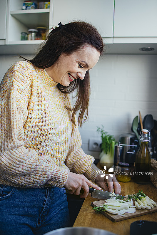 微笑的女人在现代厨房的切菜板上切茴香图片素材